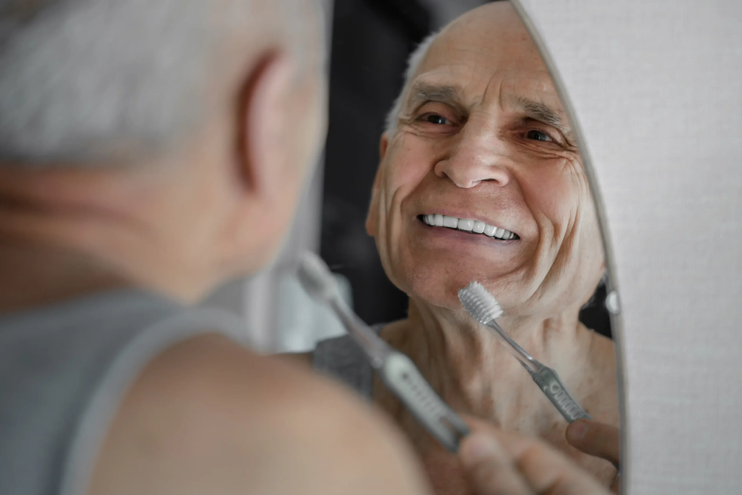 smiling senior man brushing teeth while looking in the mirror