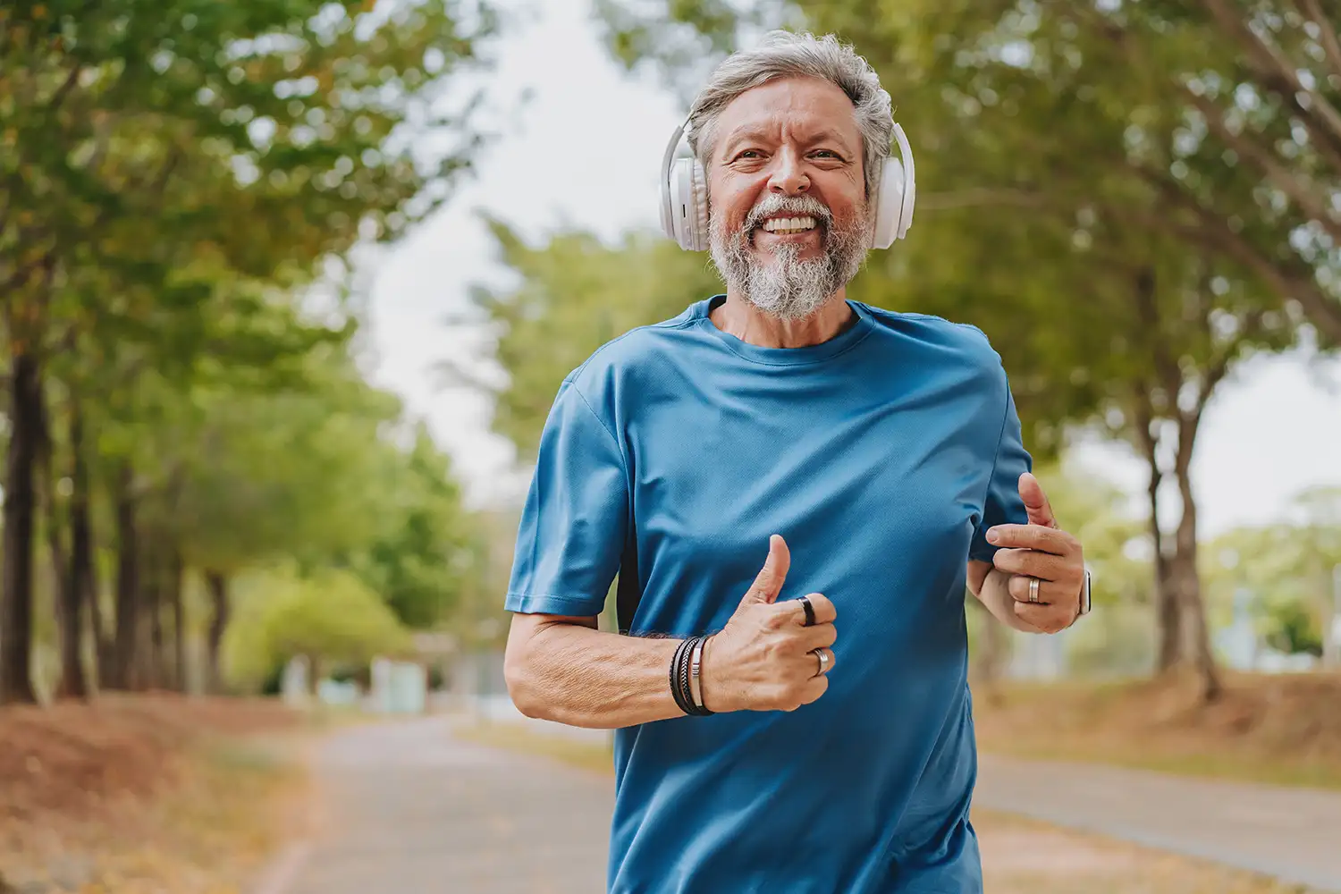 smiling senior man wearing headphones in the middle of a jog outdoors